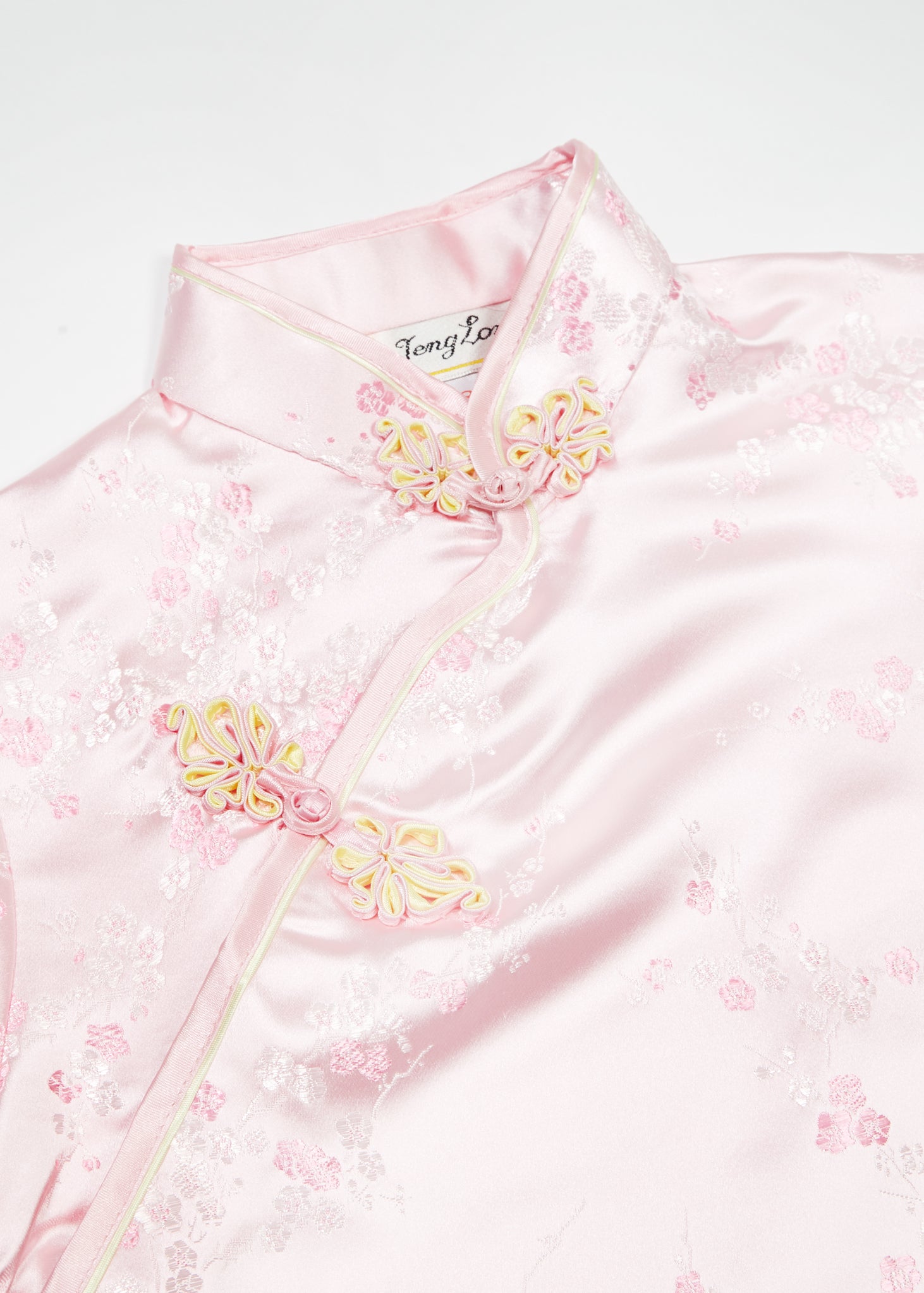 Bound edge mandarin collar and aysmmetric fastening which closes with hand stitched flower and knot frog fastenings in an accent shade. Short sleeves, side zip, curved hem into modest side splits with contrast binding and accent piping.