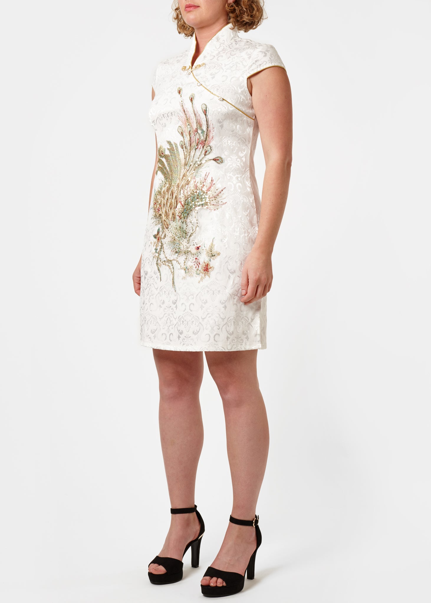 The Cheongsam or Qipao, is a feminine body-hugging dress with distinctive Chinese features of mandarin collar, side splits and hand stitched flower and knot frog fastenings. Manufactured in a classic ivory stretch cotton jacquard with a sequinned, gold embroidered peacock applique and gold piping. Invisible back zip